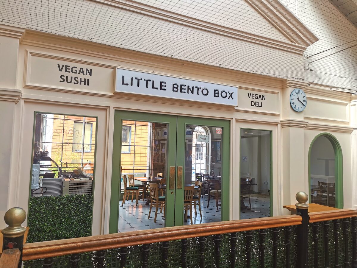 The Little Bento Box shopfront on the upstairs landing of The Gallery: cream frontage, green doors and signs reading Vegan Sushi and Vegan Deli.